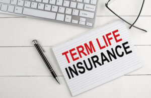 TERM LIFE INSURANCE text on notebook with keyboard , pen glasses on white wooden background
